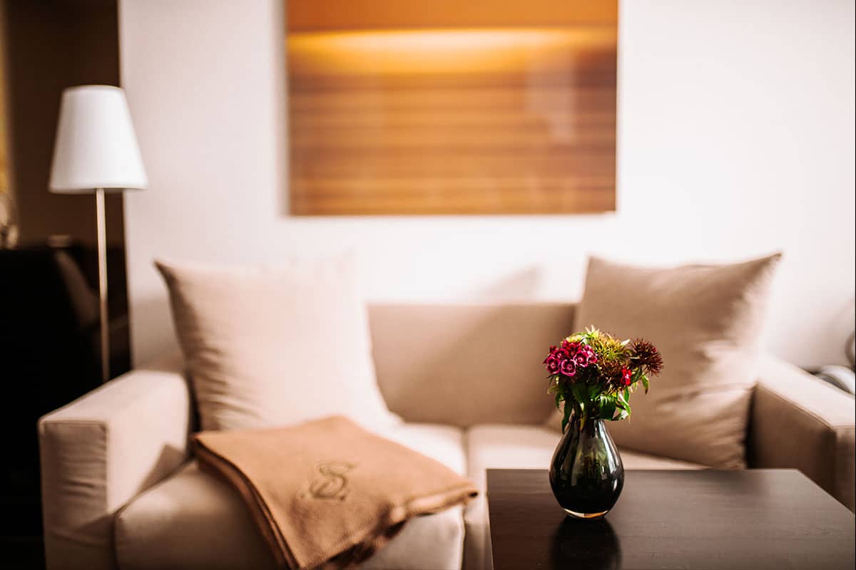 Cozy couch in the Junior Suite at the Hotel Künstlerquartier Seezeichen with an elegant blanket and fresh flowers on the table.