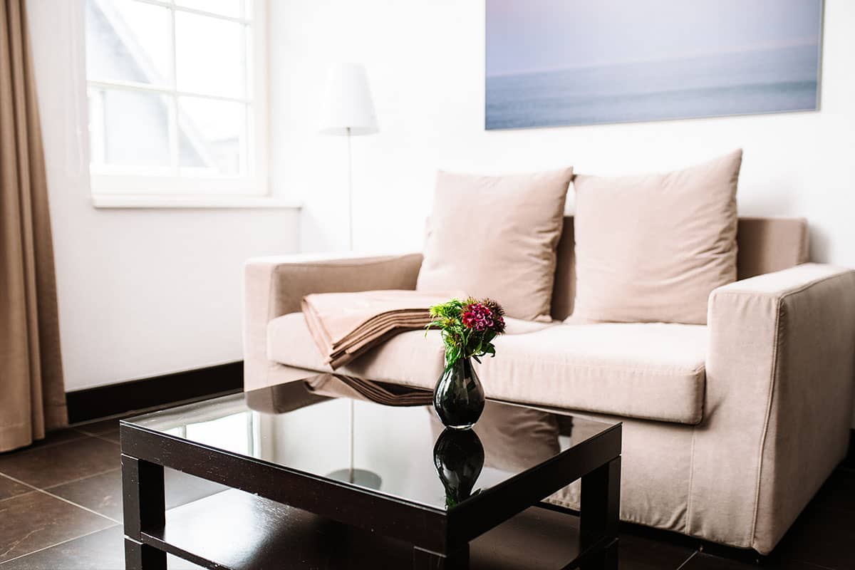 Sofa in the Junior Suite of the Hotel Künstlerquartier Seezeichen with bright design, coffee table and flower arrangement.