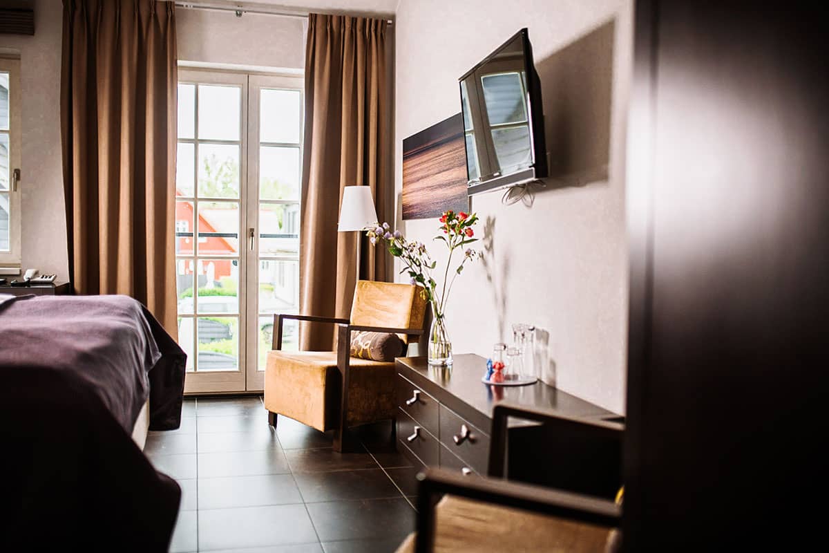 Cozy seating area with armchair, table and view through the floor-to-ceiling windows in the Comfort double room of the Künstlerquartier Seezeichen.