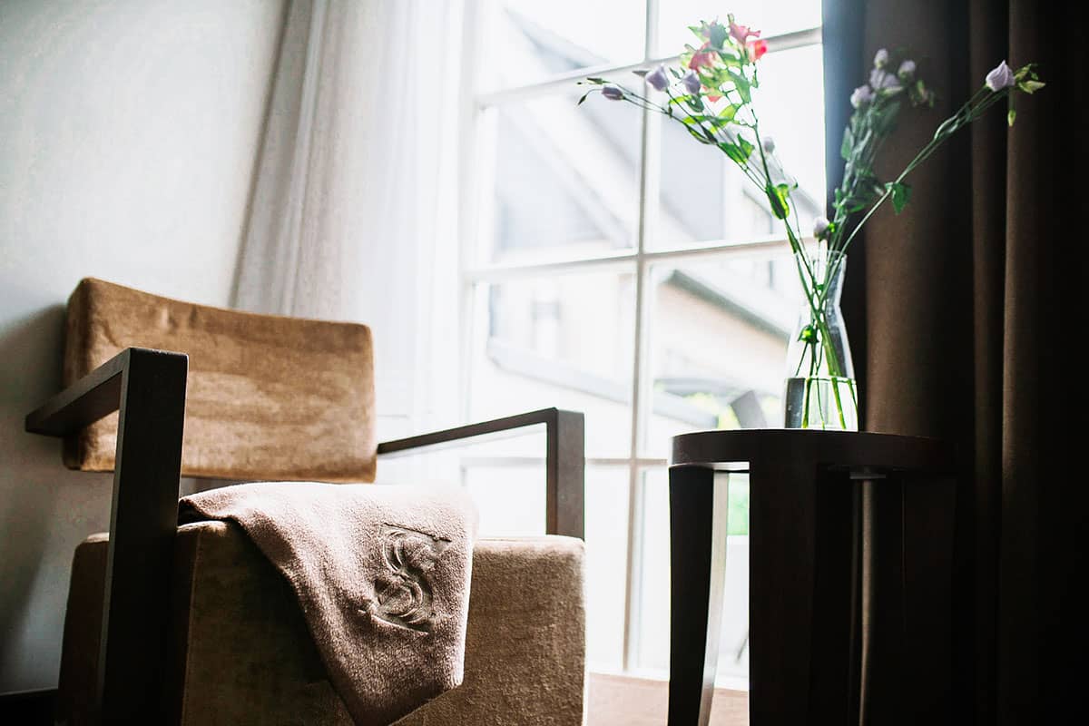 Inviting chair with decorative ceiling and side table in the bright single room of the Hotel Künstlerquartier Seezeichen.