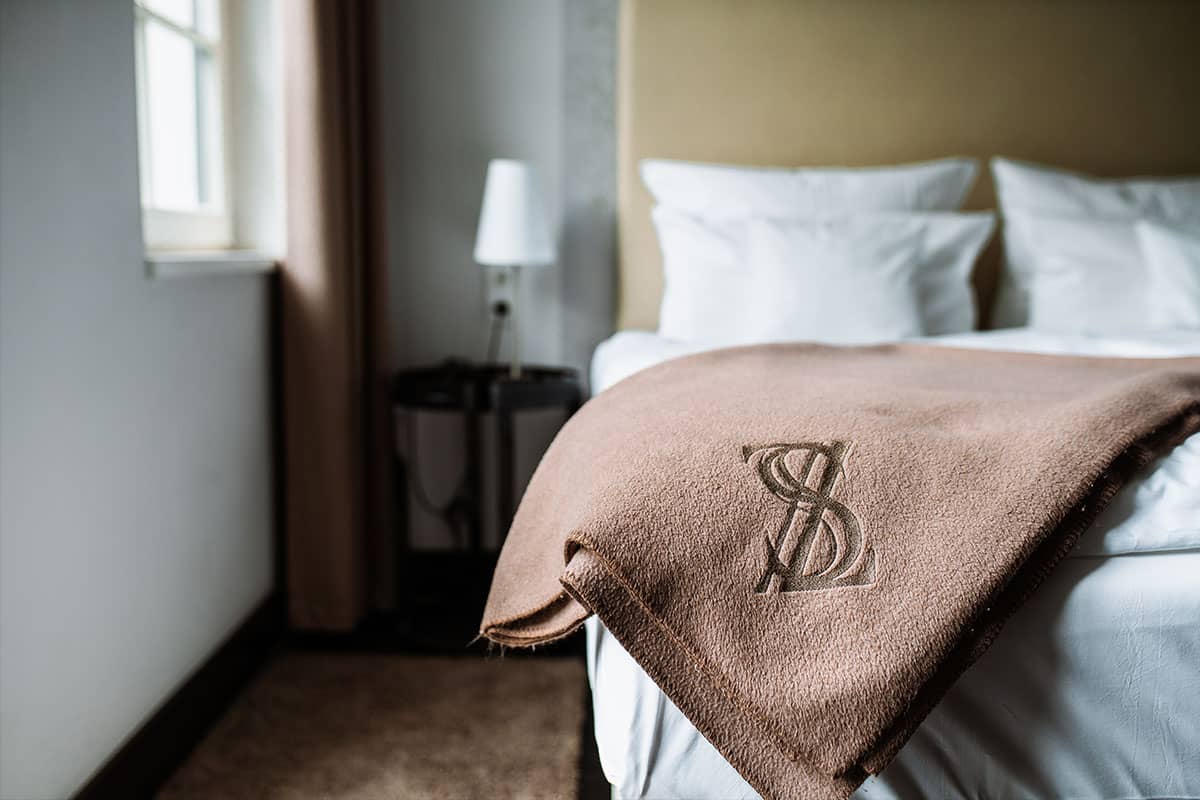 Close-up of a brown blanket with logo on a bed in a first-class double room in the Hotel Künstlerquartier Seezeichen.