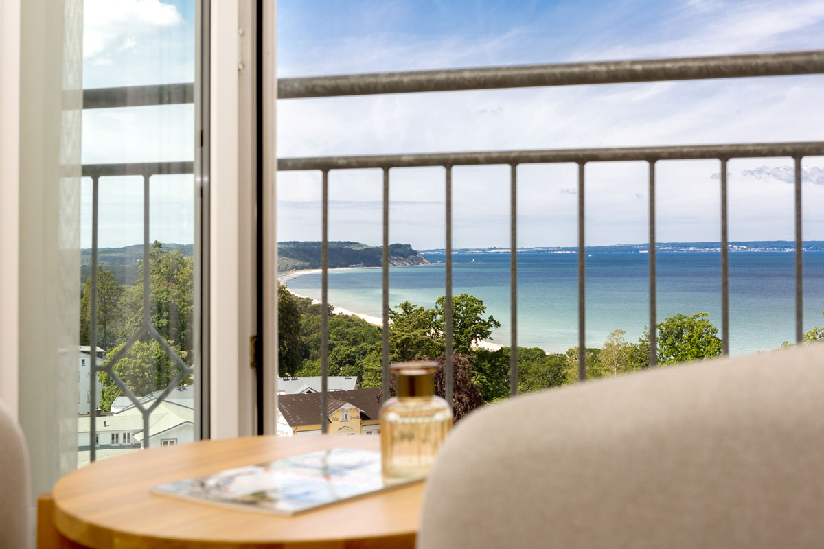 Blick vom Hotelzimmer-Balkon des Vju Hotels Rügen auf die Ostsee mit Sandstrand und grüner Küstenlandschaft.