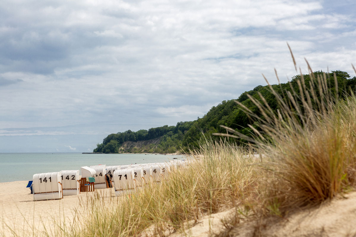 Weißer Sandstrand auf Rügen mit Strandkörben und grünen Dünen vor malerischer Steilküste im Urlaub im Vju Hotel.