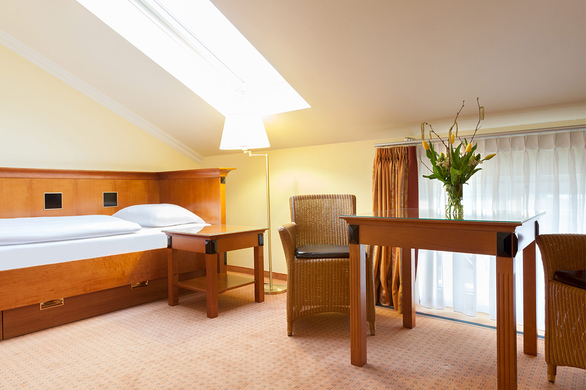 Hotelzimmer mit Einzelbett, Schreibtisch, Rattanstühlen und großen Fenstern in den Dependancen des Vju Hotels.