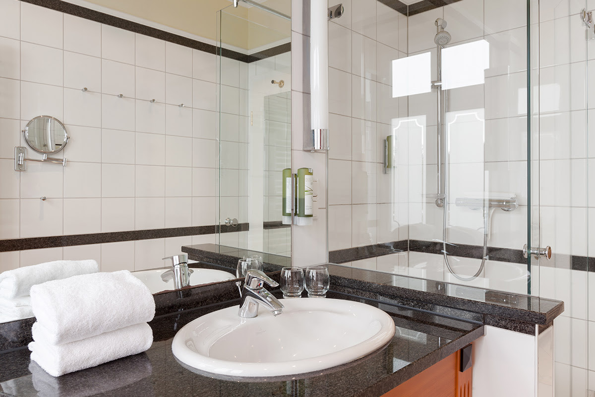 Modernes Badezimmer mit Glasdusche, Waschbecken, Spiegel und Handtüchern im Doppelzimmer der Dependancen des Vju Hotels.