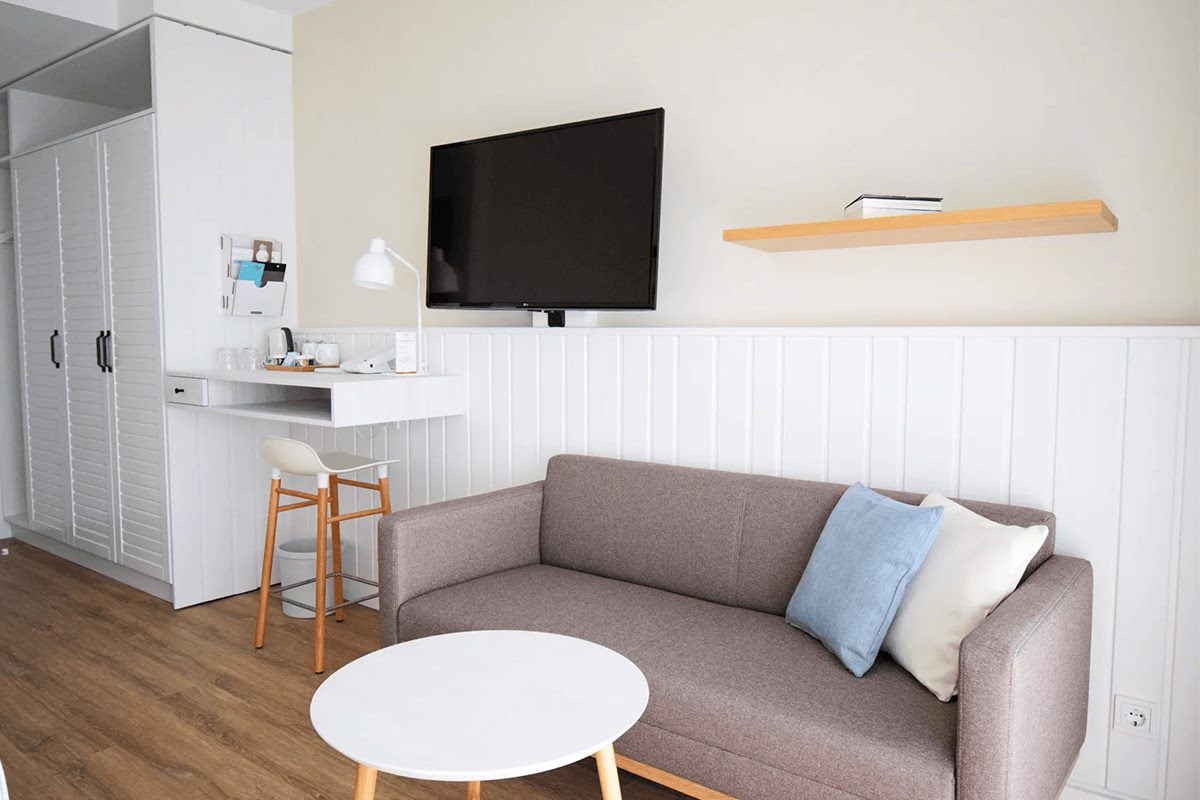 Gemütliche Sitzecke im Zimmer Buhne des Wyn. Strandhotels mit Kissen, Flatscreen-TV und minimalistischer Einrichtung.