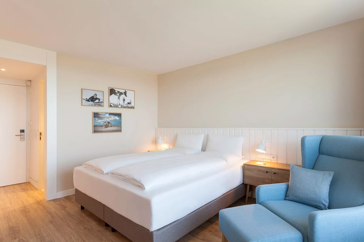 Helles Hotelzimmer Buhne im Wyn. Strandhotel mit großem Doppelbett, Nachttisch, Leselampe und gemütlichem Sessel.