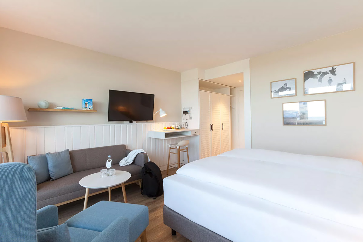 Zimmer Buhne mit großem Bett, gemütlicher Sitzecke, Wandbildern und Schreibtischbereich im Wyn. Strandhotel auf Sylt.