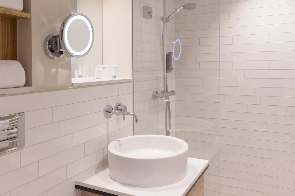 Modernes Badezimmer mit rundem Waschbecken, Glasdusche und beleuchtetem Kosmetikspiegel im Zimmer Buhne des Wyn. Strandhotels.