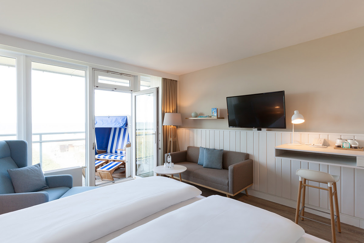 Modern eingerichtetes Hotelzimmer Buhne mit Sofa, TV und Zugang zum Balkon mit Strandkorb im Wyn. Strandhotel.