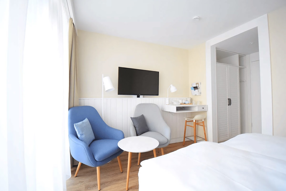 Heller Sitzbereich im Hotelzimmer "Land in Sicht" im Wyn. Strandhotel mit zwei Sesseln, Beistelltisch und Tageslicht.