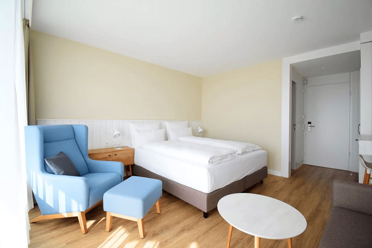 Helles, modern eingerichtetes Muschelsucher-Zimmer mit gemütlichem Bett und blauem Ohrensessel im Wyn. Strandhotel.