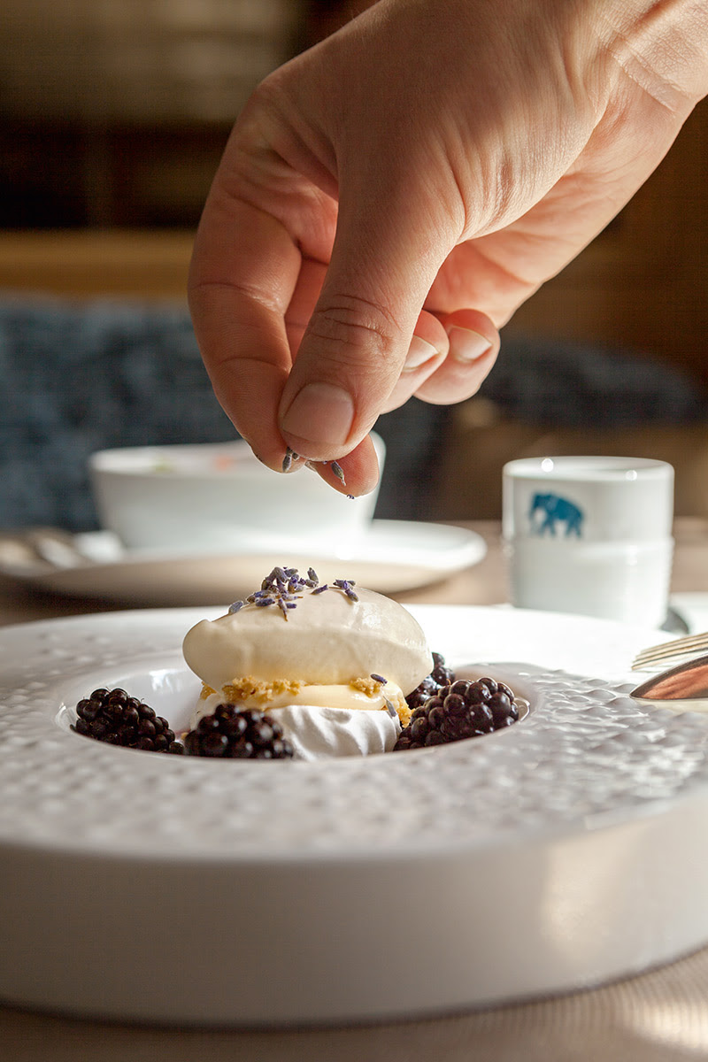 Hand verfeinert ein Dessert mit frischen Brombeeren und Sahne auf einem elegant angerichteten Teller.