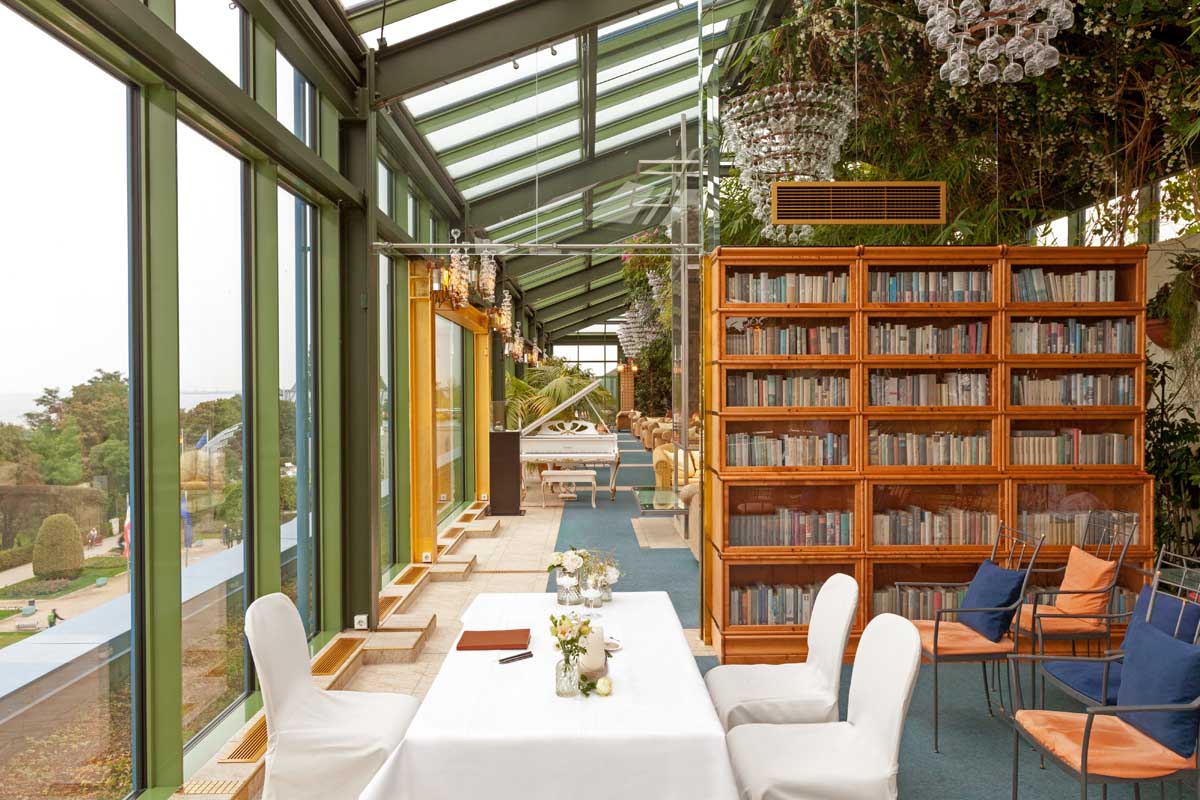 Salon Tucholsky im Kaiserhof Heringsdorf auf Usedom, ausgestattet mit Bücherschränken, Tischen und Panoramafenstern zum Meer.
